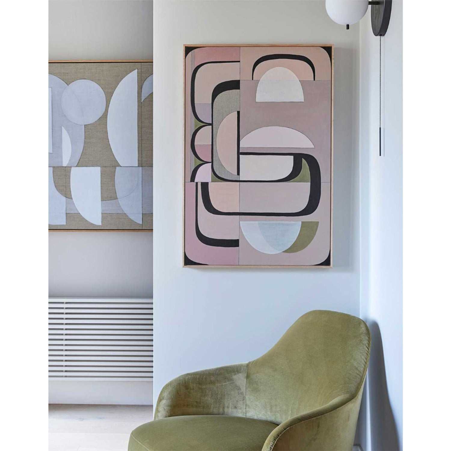 Framed Giclee print featuring geometric shapes in dusty pink, olive green, and muted gray tones, with bold magenta arcs, displayed above a modern green chair in a well-lit room.